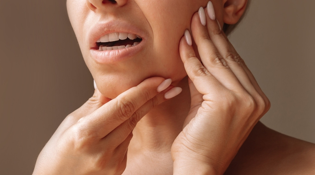 Woman holding jaw and cheek due to TMJ pain and jaw tension discomfort.