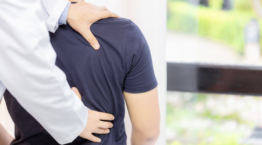 Chiropractor discussing a chiropractic treatment plan while evaluating a patient's back and shoulder movement during an office visit.